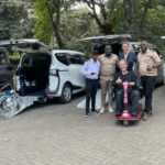 Bryce gives a thumbs up from his red powered mobility scooter, with the Accessible Travel Kenya team in front of four wheelchair-accessible vans with their ramps lowered