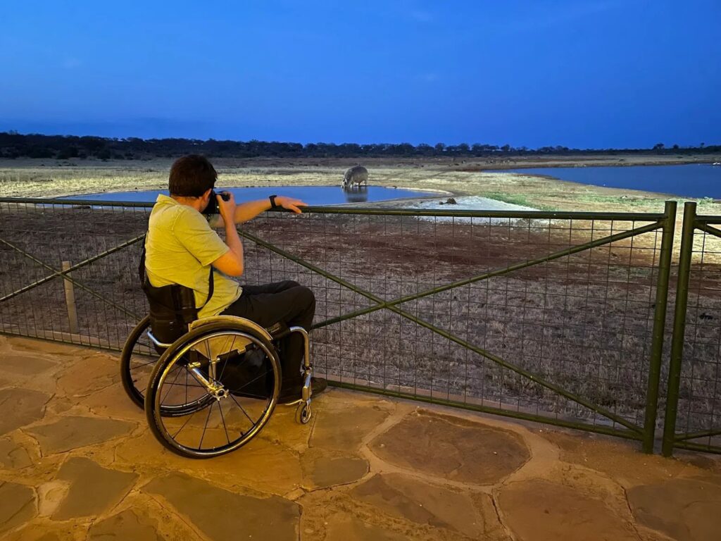 Wheelchair user photographing a hippo at the waterhole at Kiboko River Camp