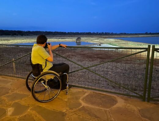 Wheelchair user photographing hippos at a waterhole on safari